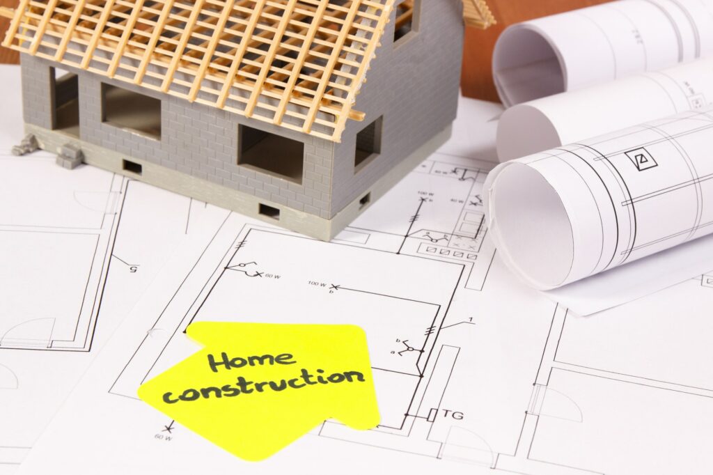 house under construction and rolls of electrical diagrams or blueprints building home concept